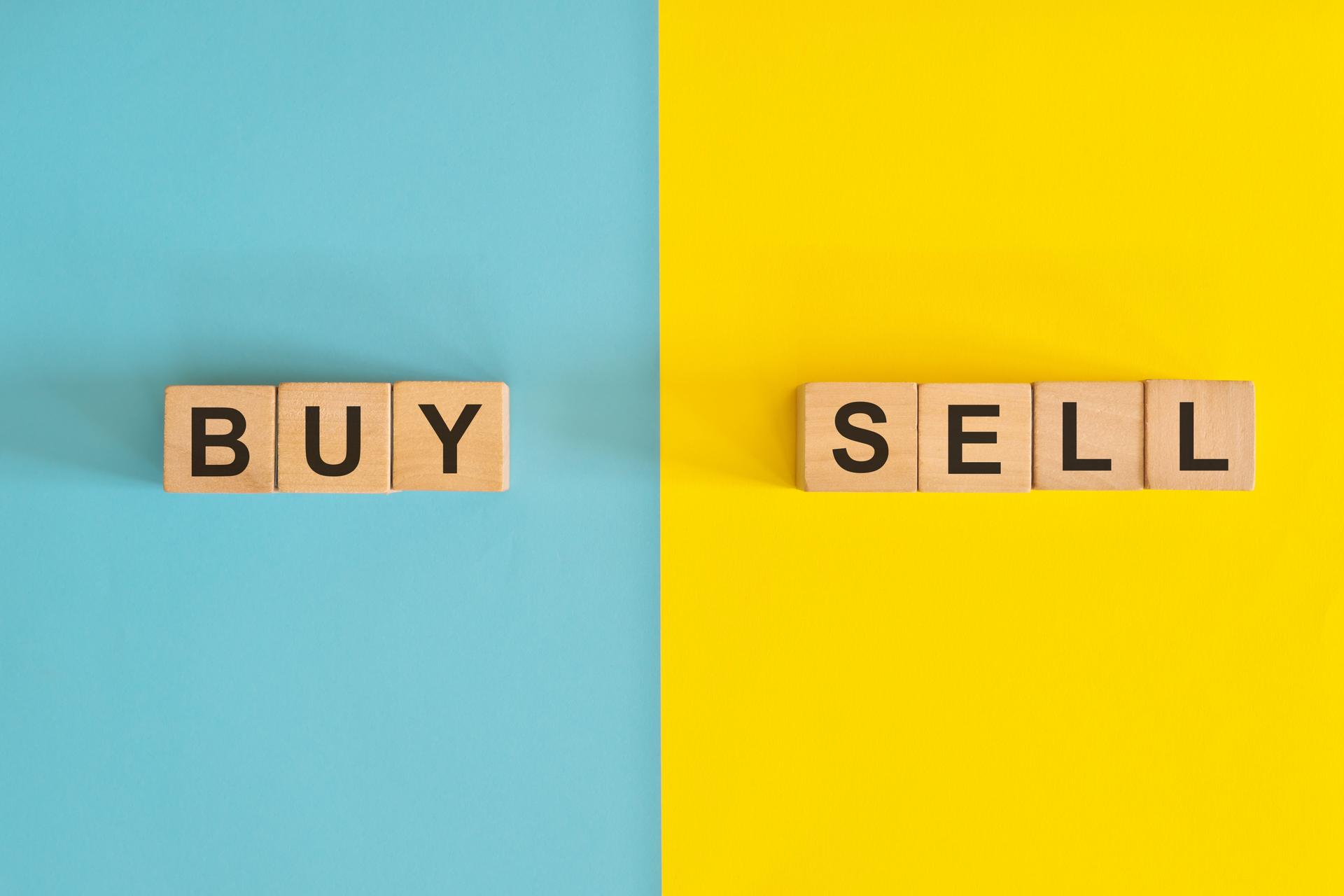 Buy versus sell in business and investing concept. Wooden blocks typography in bright blue and yellow background.